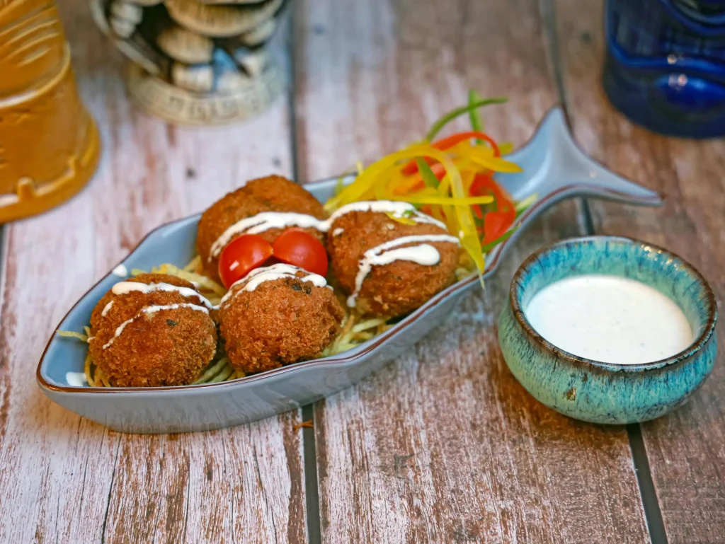 Conch fritters on a blue dish with sauce and vegetables