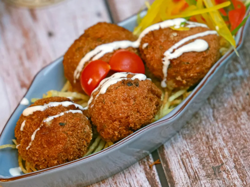 Conch fritters on a blue dish with sauce and vegetables