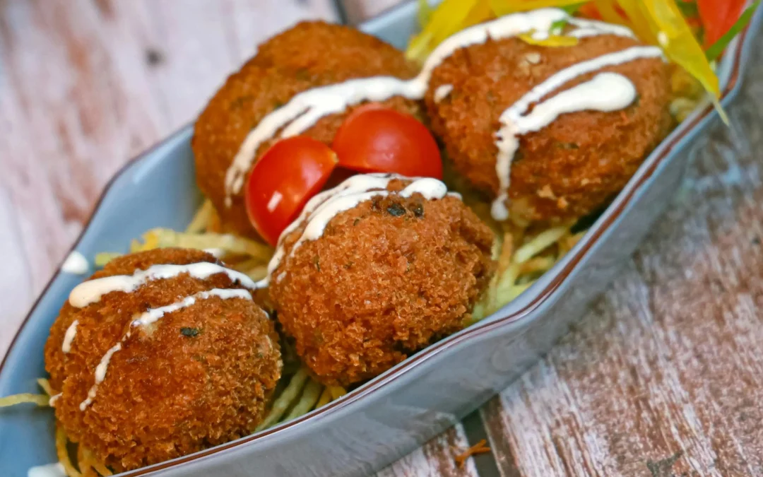 Conch fritters on a blue dish with sauce and vegetables